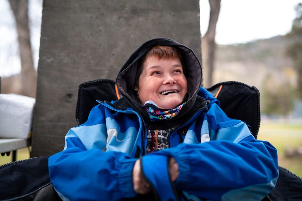 Person using a wheelchair with a blue jacket on smiles up towards the sky